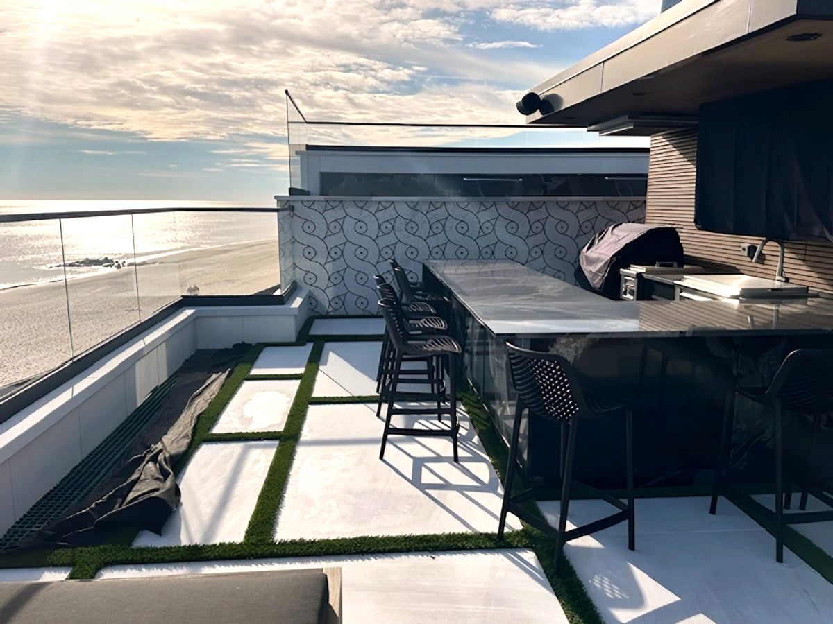 Rooftop outdoor kitchen with bar stools and artificial turf pavers beside the beach